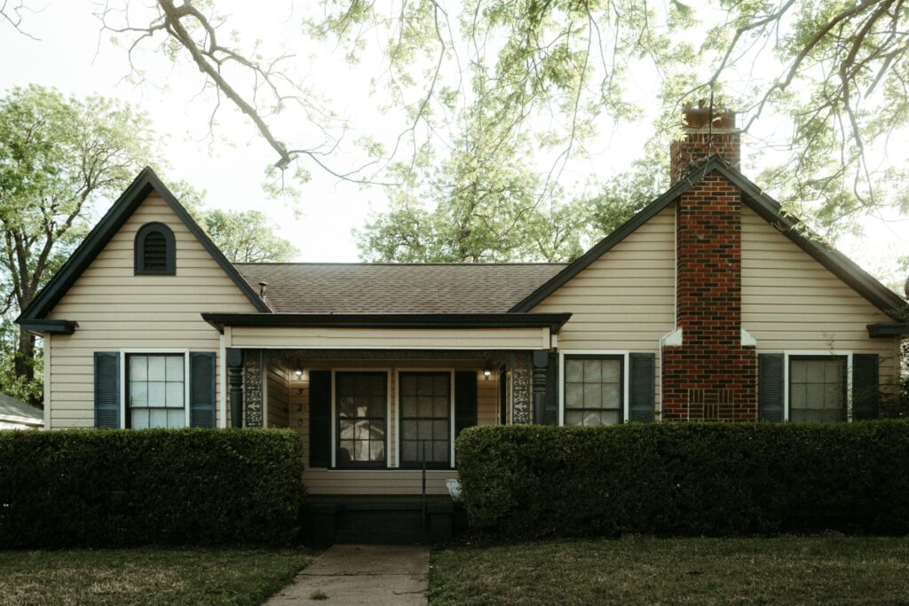 Beige suburban house with brick chimney and hedges