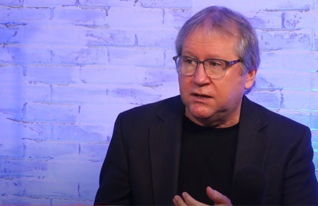 Man speaking in studio with brick wall backdrop