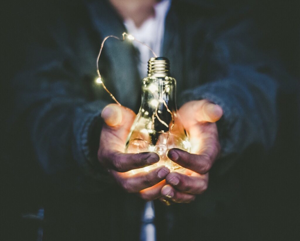 Hands holding glowing light bulb with fairy lights