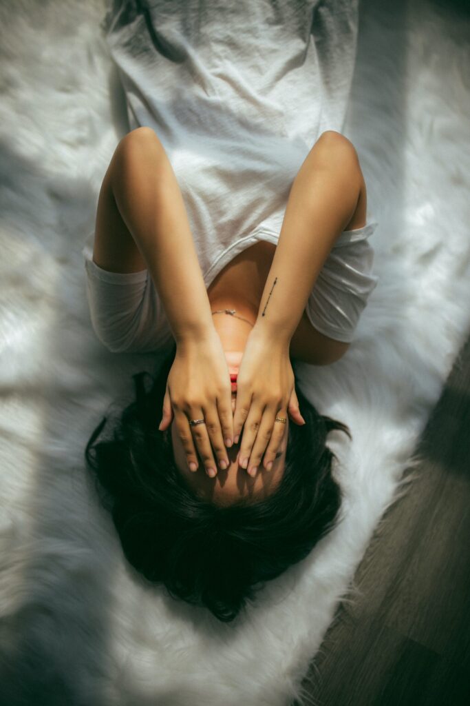 Woman lying on white rug covering face