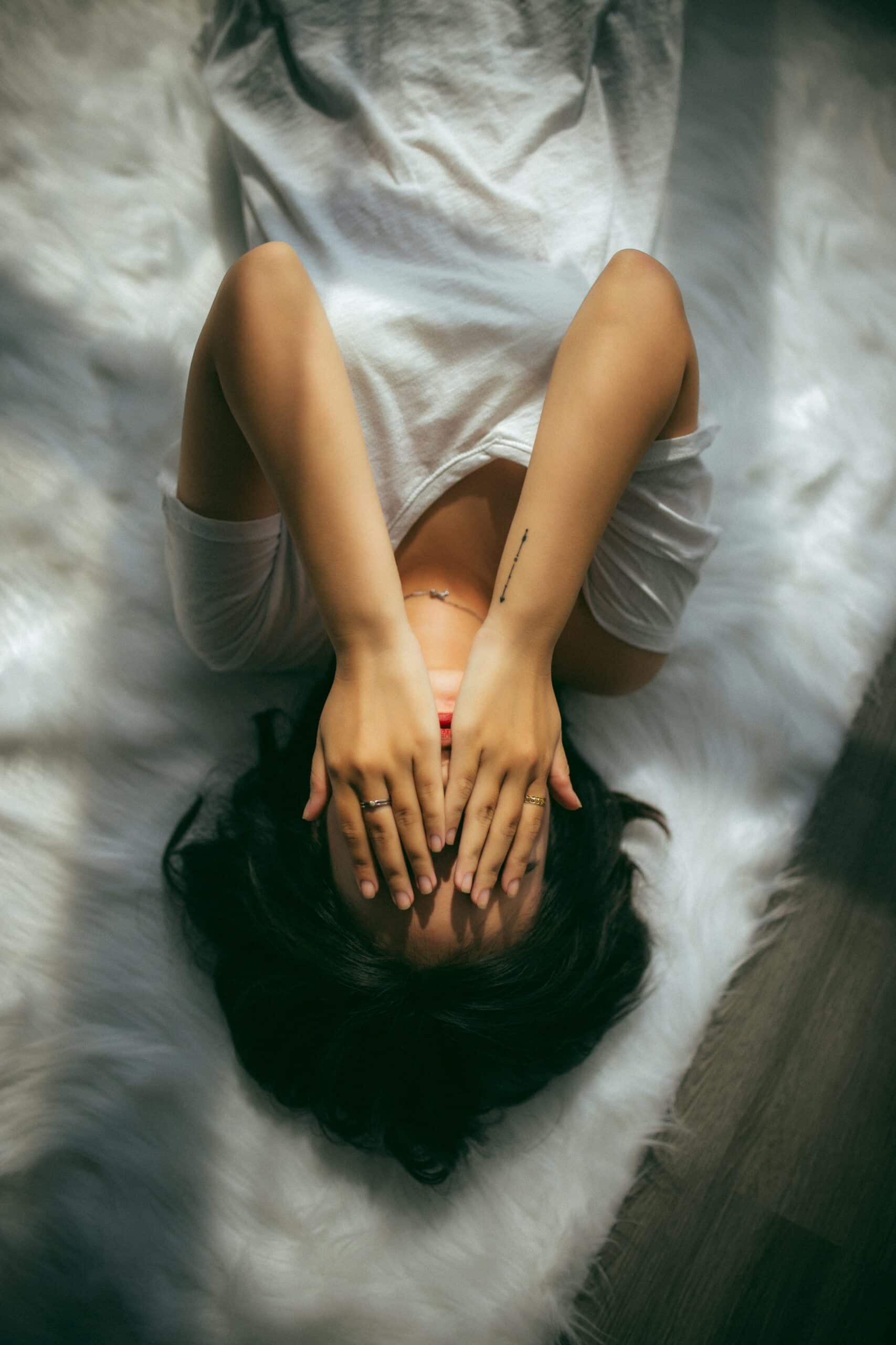 Woman lying on white rug covering face