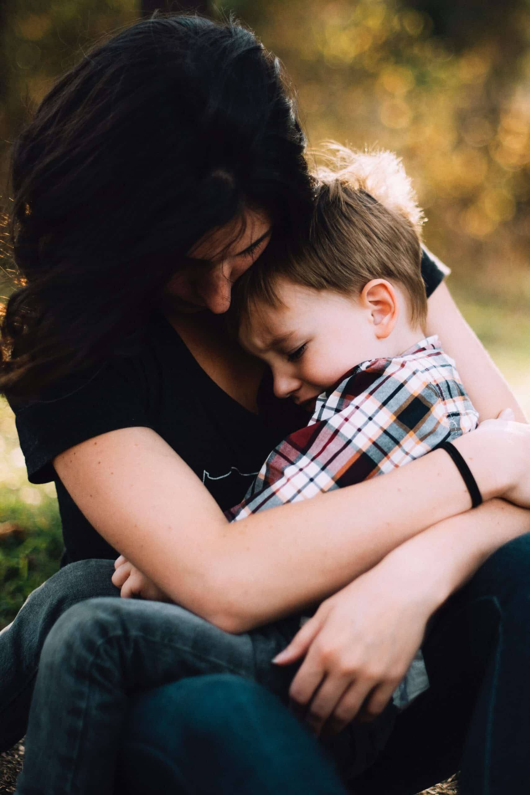 Mother hugging young son outdoors at sunset