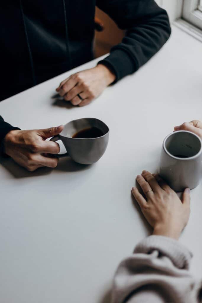 Two people holding coffee mugs at table