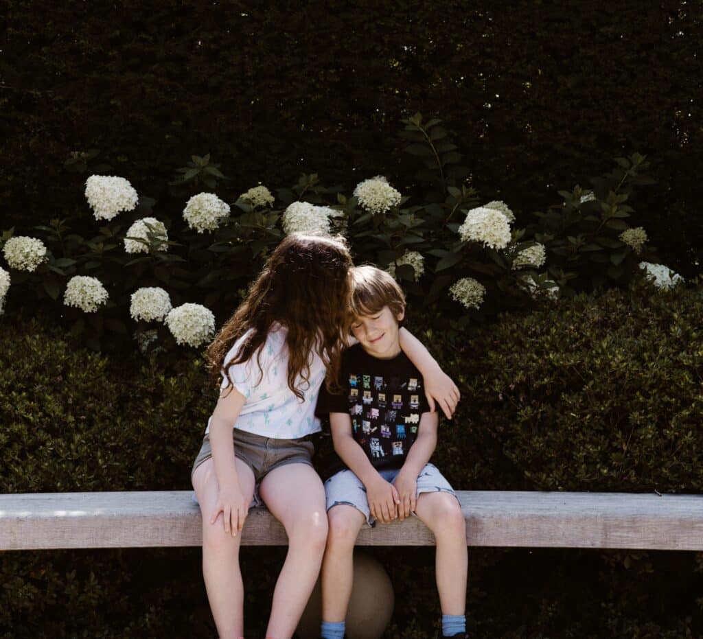 Two children hugging on bench by white flowers
