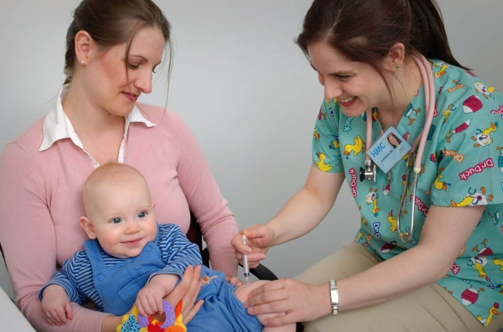 Nurse administering vaccine to baby held by mother