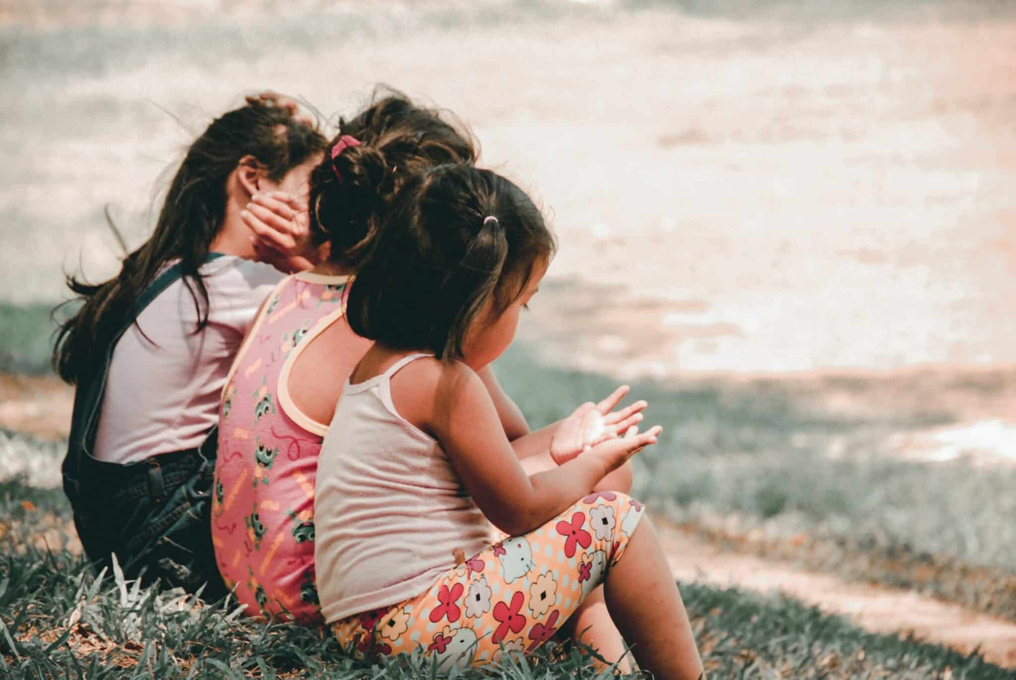 Three young children sitting together on grass outdoors