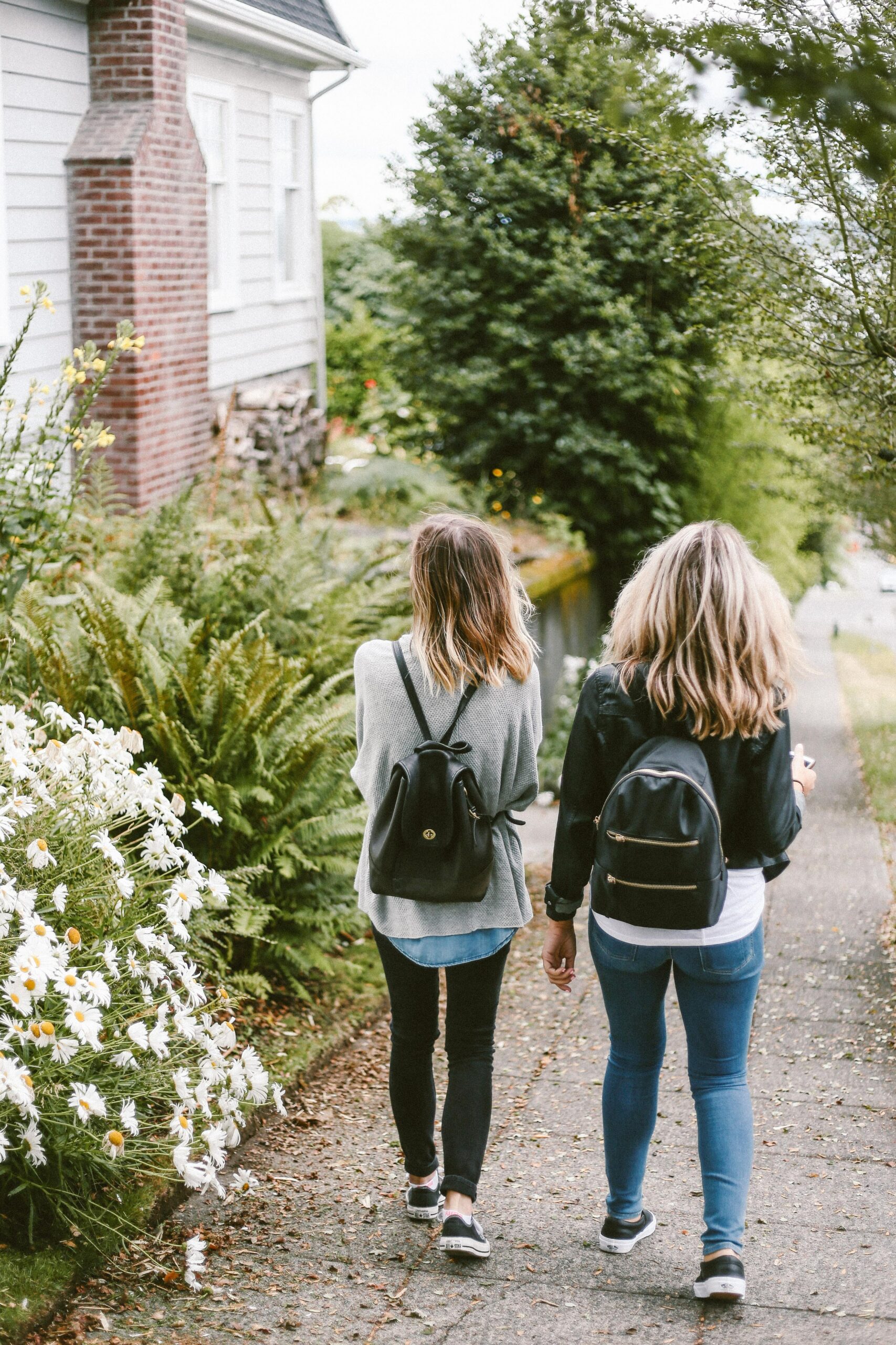 Two women walking down leafy neighborhood sidewalk