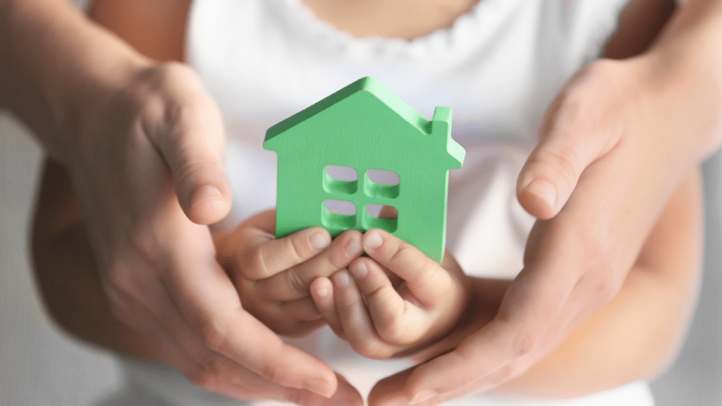 Child holding green house model with adult hands