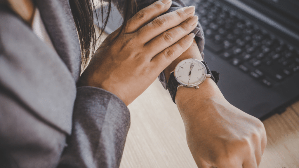 Person checking wristwatch beside laptop on desk