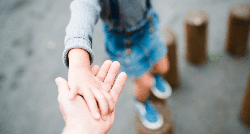 Child holding adult's hand while walking outdoors