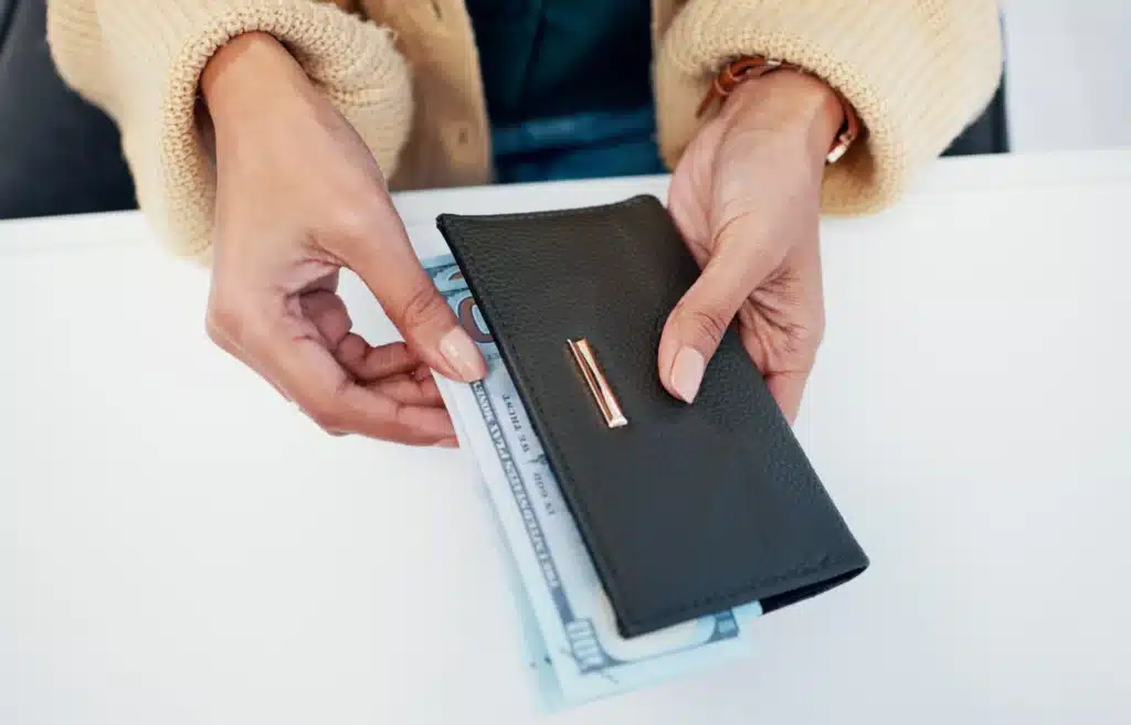 Hands pulling cash from black leather wallet