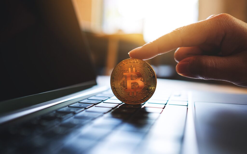 Hand touching Bitcoin coin on laptop keyboard